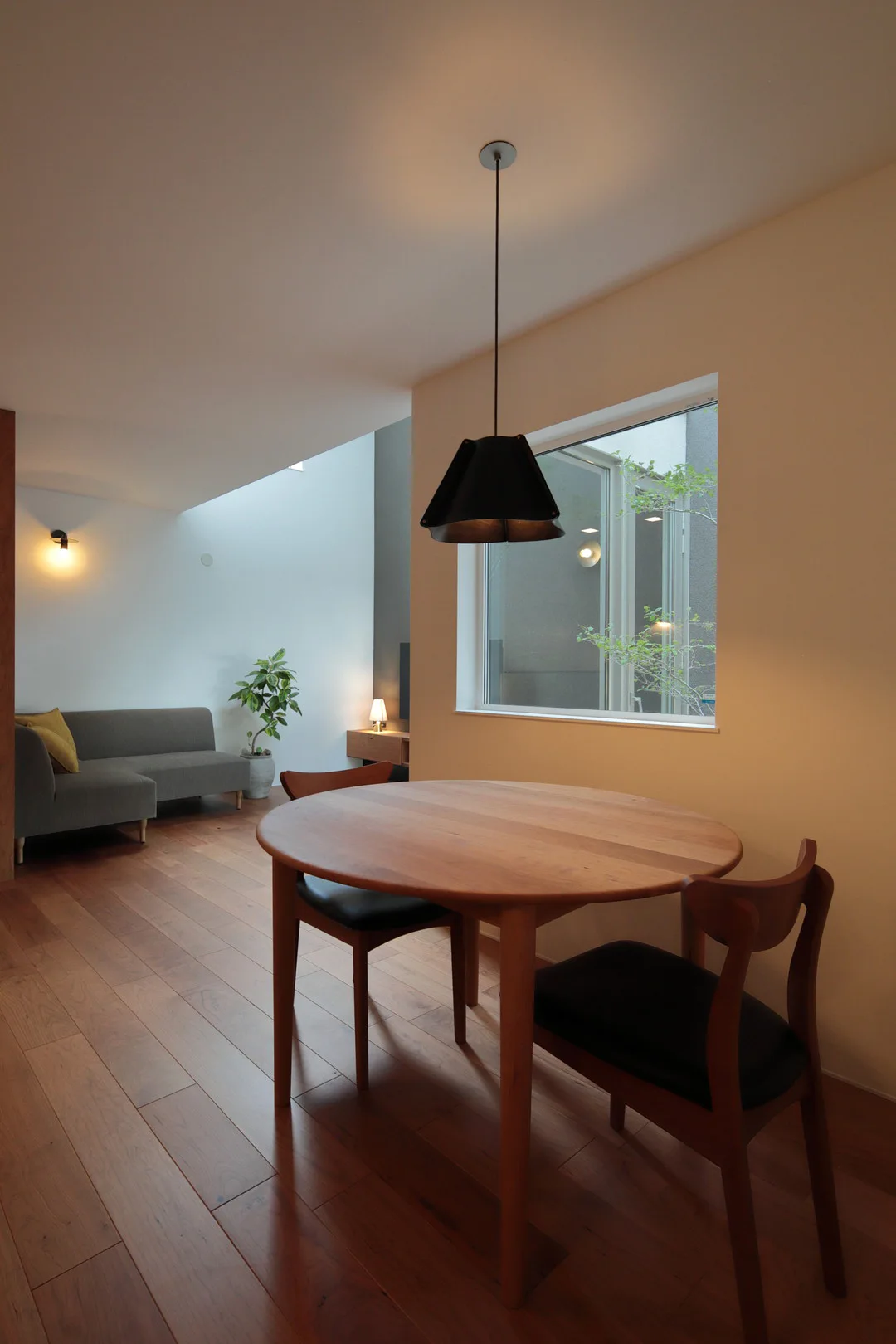 円形テーブルを照らす黒いペンダントライトと、奥に見えるソファのあるくつろぎ空間