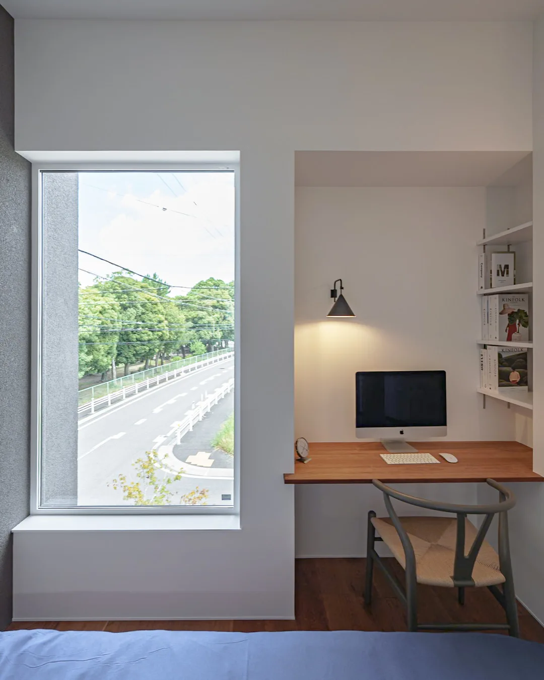 外の緑豊かな通りを一望できる窓と、その横にあるパソコンデスクと壁面収納
