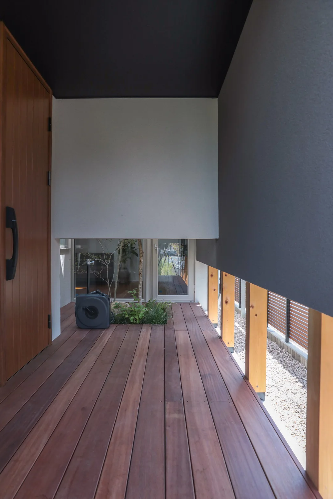 3方が壁で囲われ、軒がある玄関ポーチ。木製のデッキ床と、低い位置の開口部から外の緑が見える半屋外空間