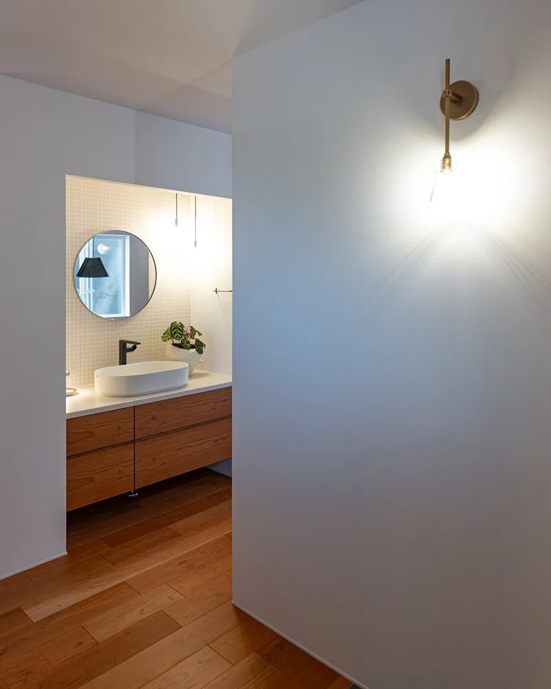 丸い鏡とチェリー材のキャビネットがおしゃれな洗面台と、壁面を温かく照らすブラケットライト