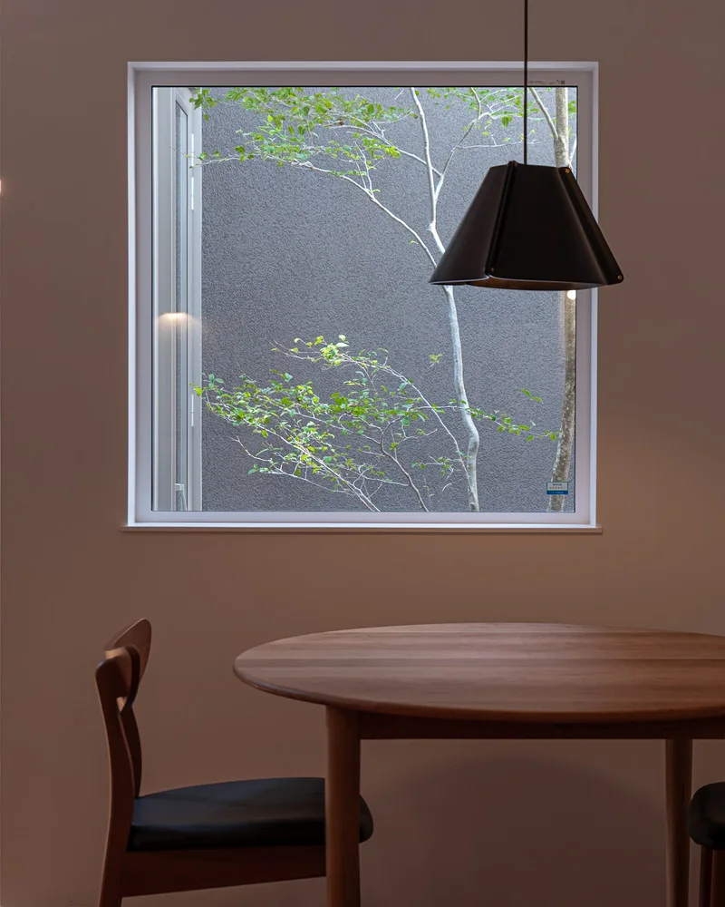 丸い木製ダイニングテーブルと黒いペンダントライトのある、ピクチャーウィンドウから緑の風景が見えるダイニング