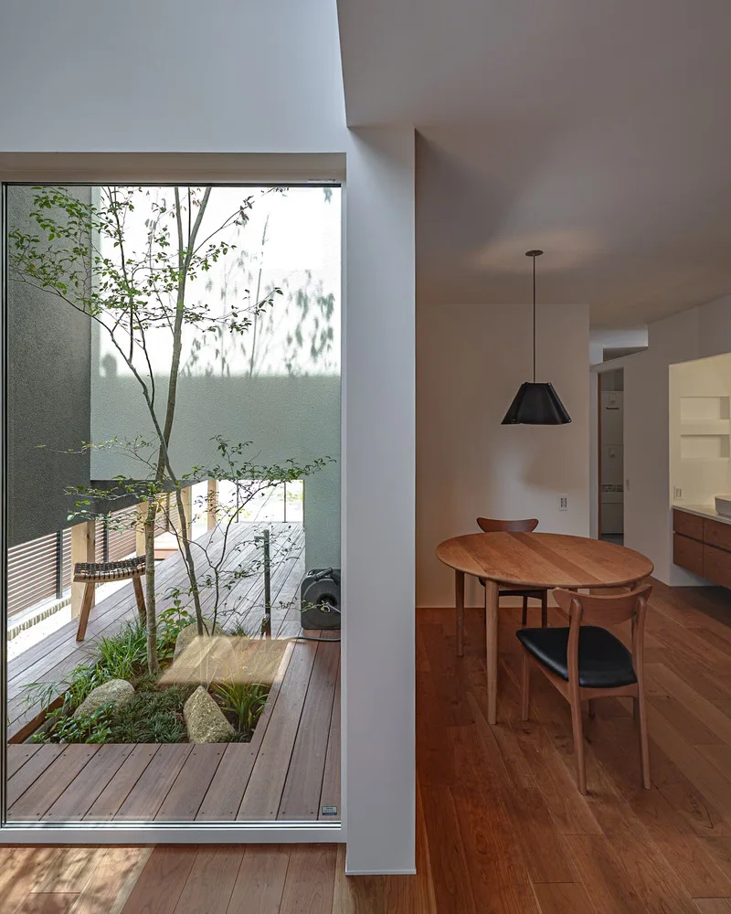 吹き抜けから明るい光が差し込む中庭と、無垢材のフローリングが続くリビング