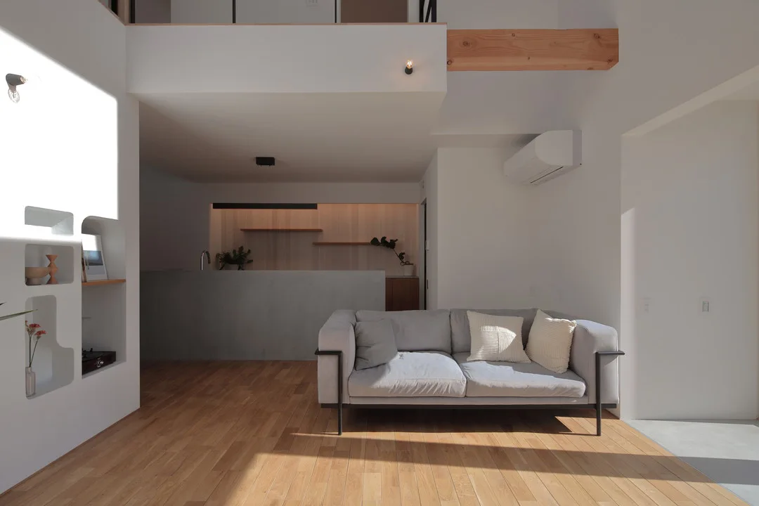 グレーのソファが置かれたリビングと、その奥に続くモールテックス腰壁のキッチンスペース